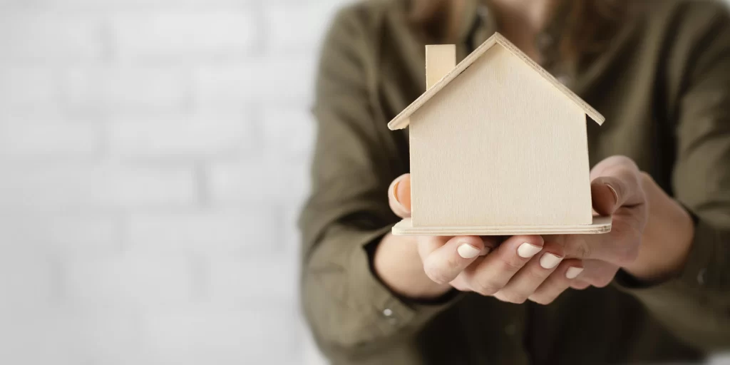 Mujer sostiene una casa de madera.