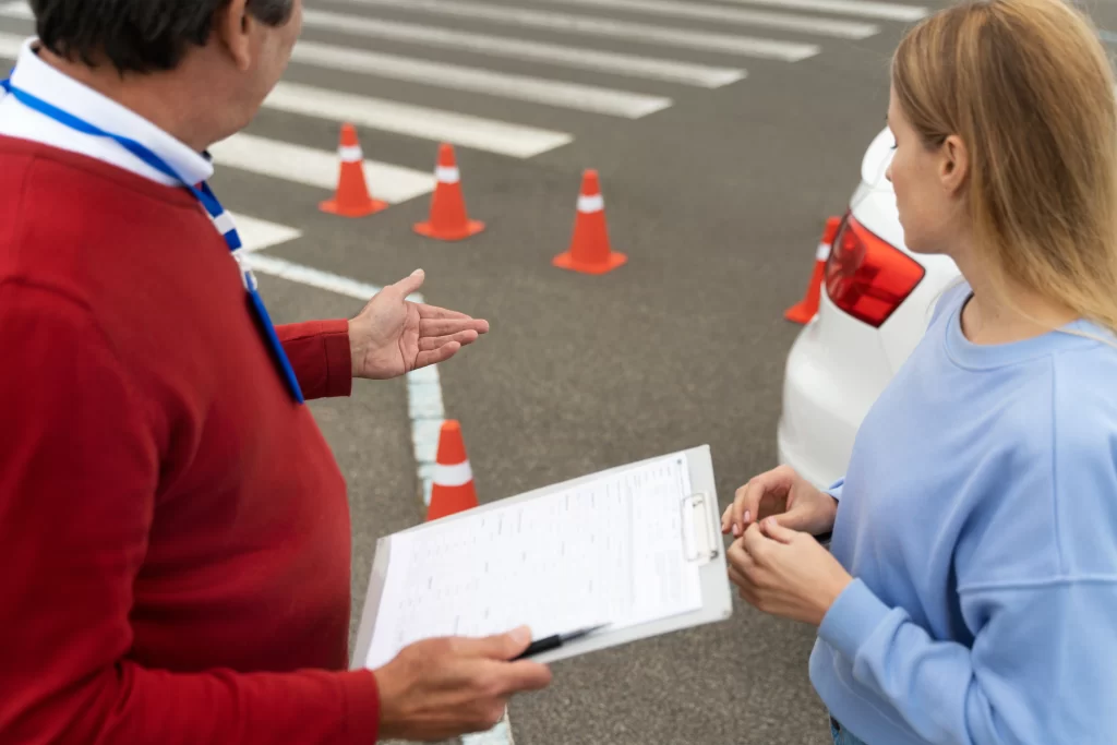 Instructor de manejo charla con una mujer y ambos miran los conos de precaución de la carretera.